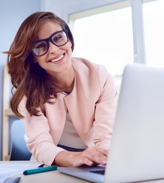 Smiling woman with glasses typing on laptop