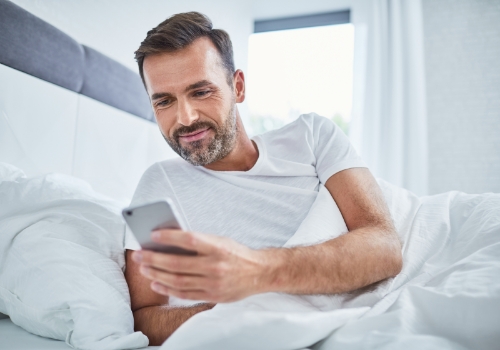 Smiling man laying in bed looking at his phone