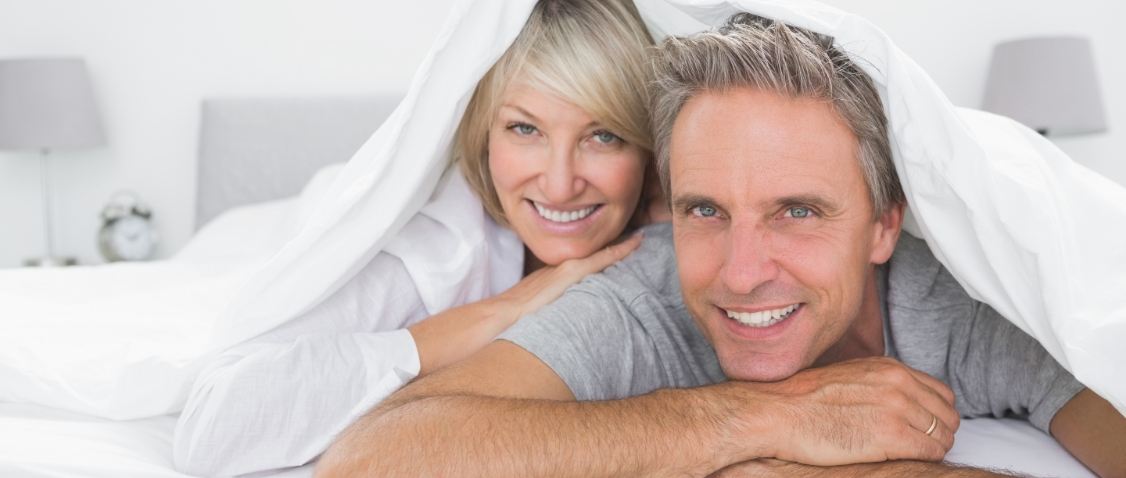 Older man and woman laying in bed on their stomachs and smiling after sleep apnea services in Scottsdale