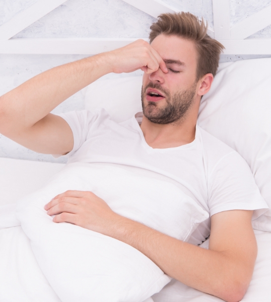 Man in bed pinching bridge of nose needing sleep apnea treatment in Scottsdale