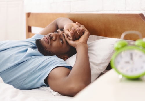 Man lying awake in bed with alarm clock on nightstand