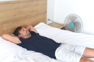 Man sleeping on bed next to a fan